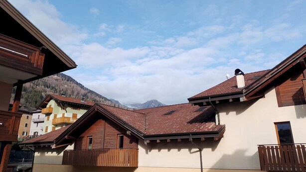 Un borgo montano con case in legno tradizionali, balconi e un cielo sereno.