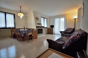 A living room with a sofa, a dining table with chairs, a fireplace, and a television.