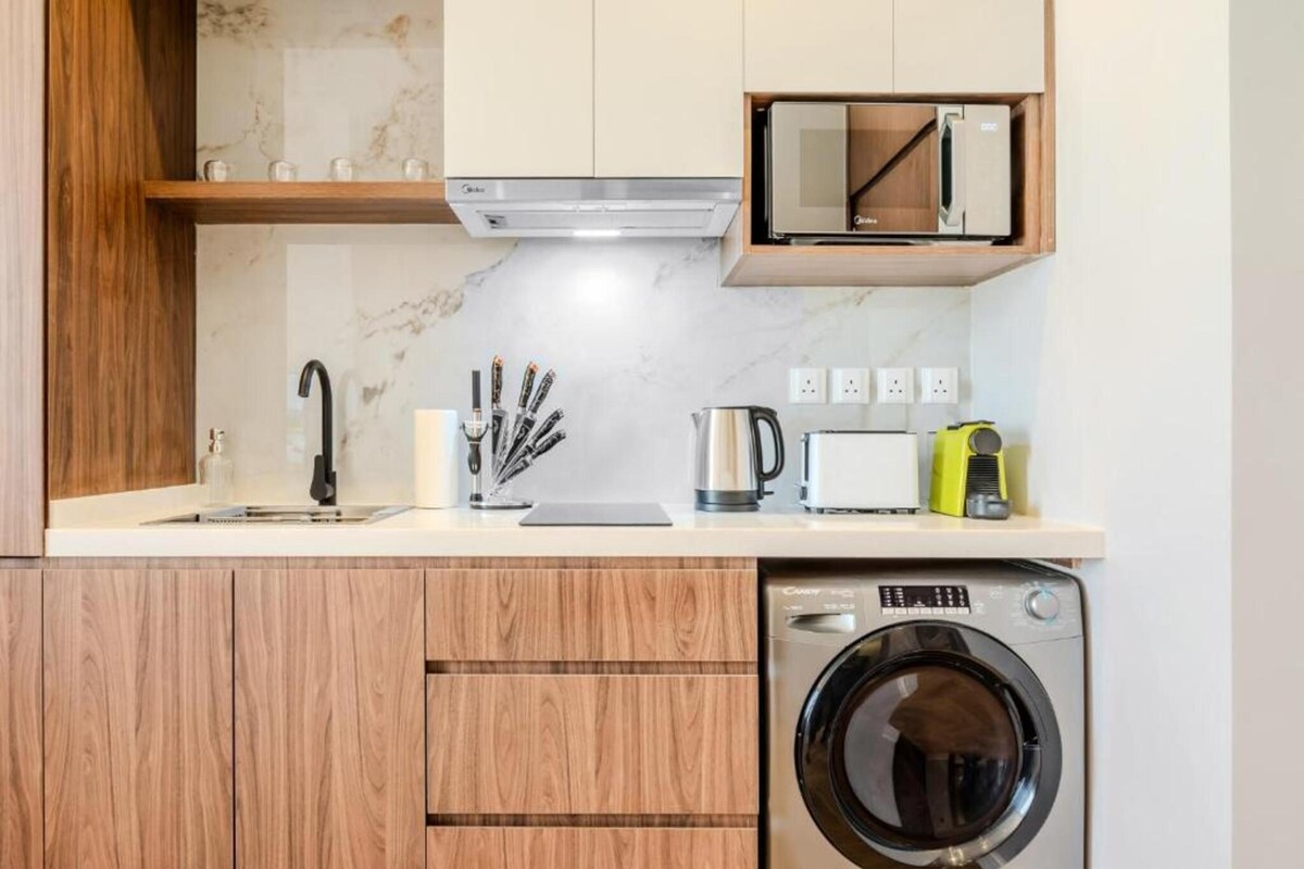 A compact kitchen with wooden cabinets, a microwave, a coffee maker, and a washing machine.