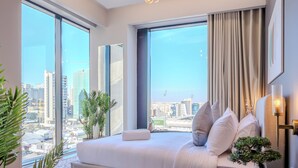 A modern hotel room with a large bed, a city view, and a potted plant.