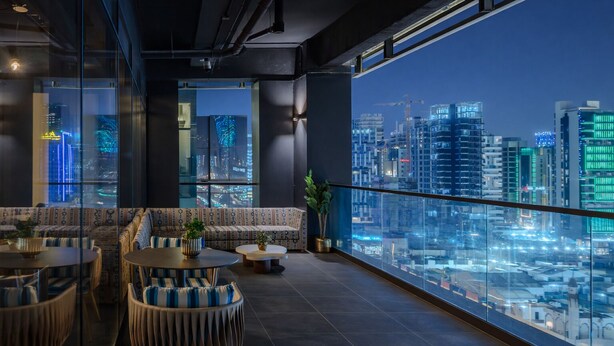 A modern lounge with a city view, featuring a sofa set, round tables, and potted plants.