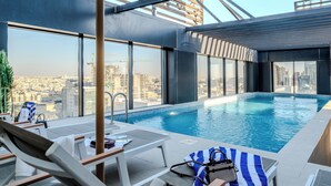 A rooftop infinity pool with lounge chairs and a view of the cityscape.