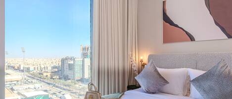 A hotel room with a bed, a view of the city, and a large window.
