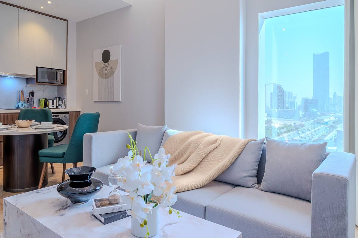 Uma sala de estar moderna com um sofá, mesa de centro e vista para a paisagem urbana através de uma grande janela.