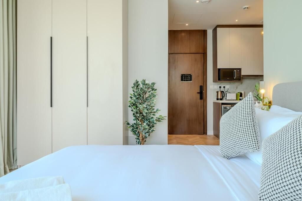 A hotel room with a bed, a small kitchenette, a wooden door, and a potted plant.