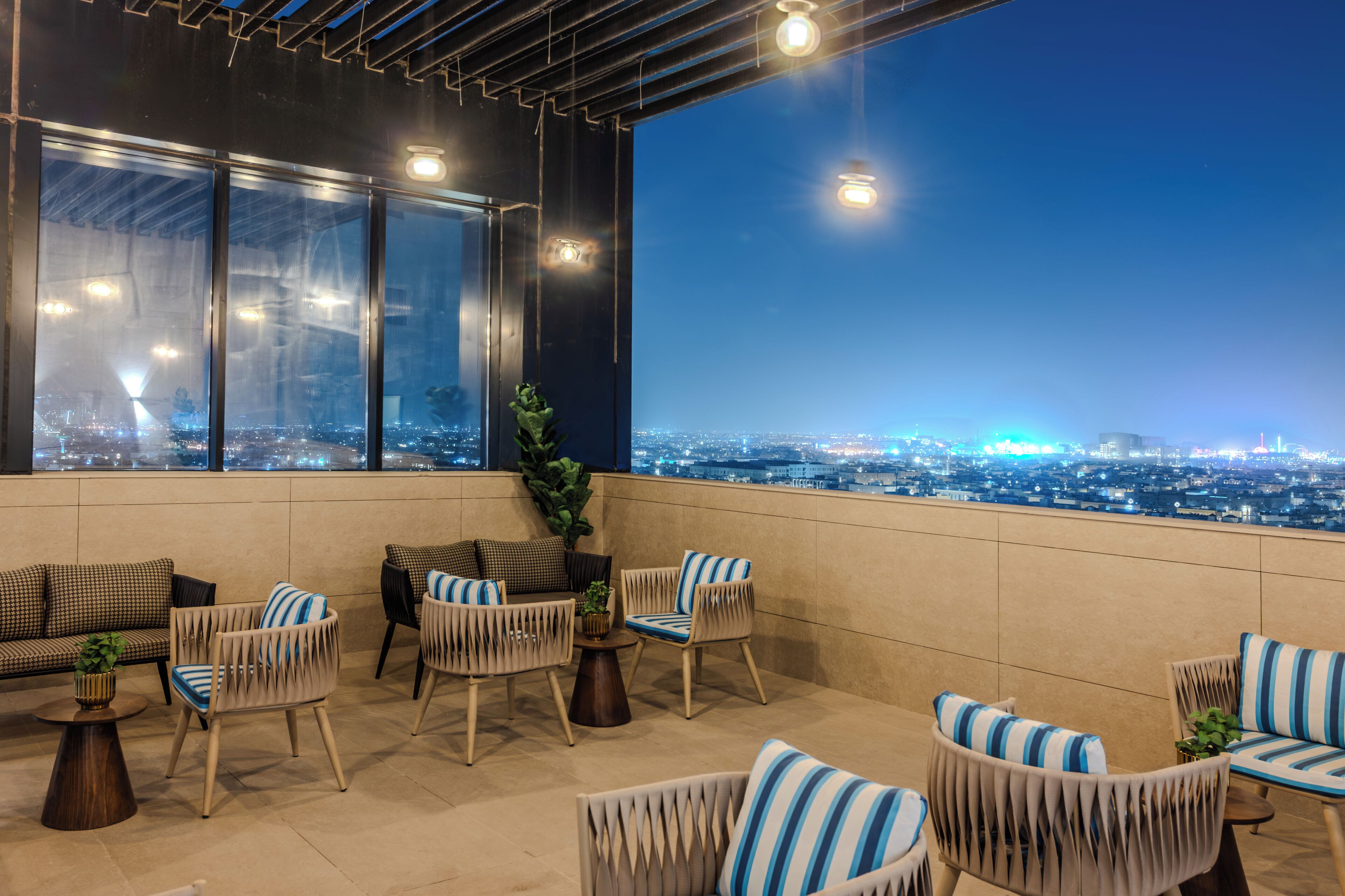 Un salón en la azotea con asientos, vistas de la ciudad y ventanas amplias.
