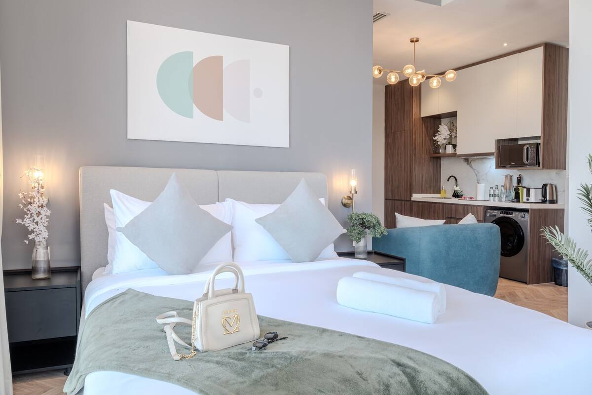 Quarto moderno com cama, mesa de cabeceira e vista para a cozinha.