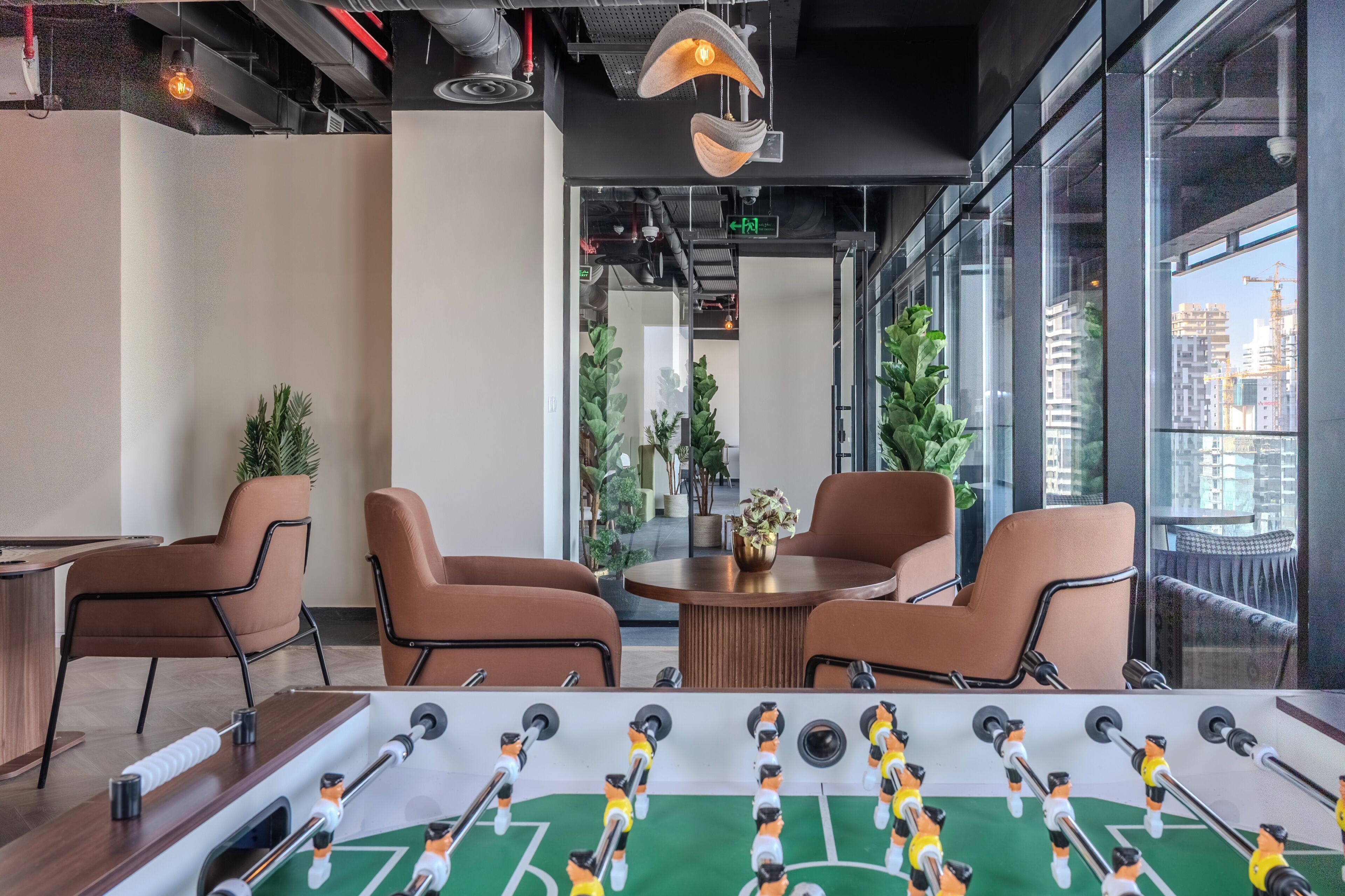 A modern indoor space with a foosball table, leather chairs, and a view of the city through large windows.