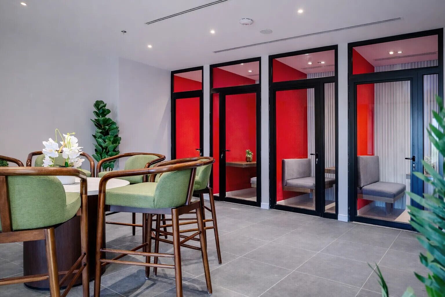 A modern dining area with a table and chairs, a potted plant, and a red accent wall.