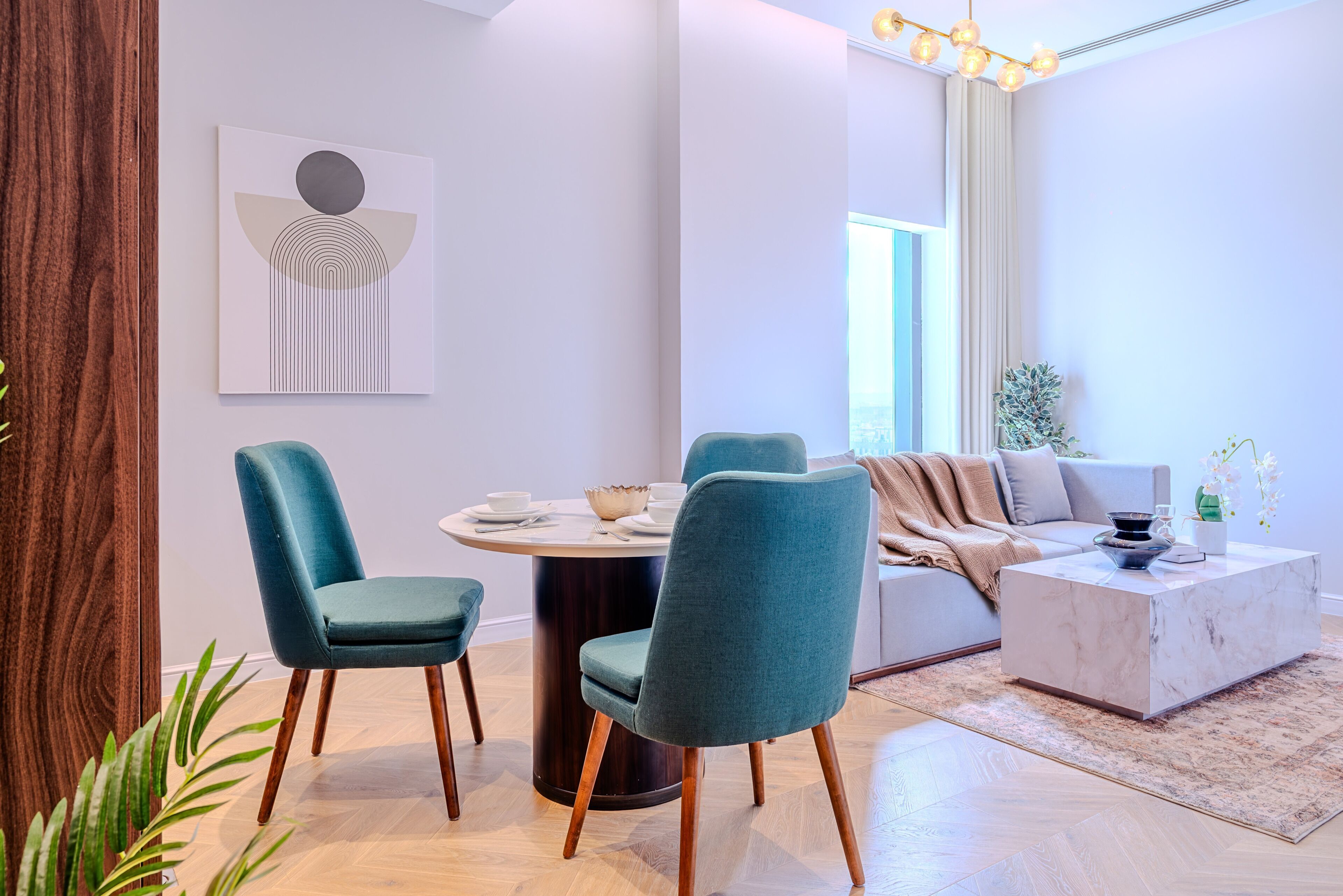 A modern living room with a round dining table, teal chairs, a sofa, and a coffee table.