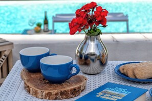 A table with two blue cups, a silver vase with red flowers, a plate with cookies, and a book titled "Fifth Avenue, Fifth Street." - Villa Angiolina - Ideal for 5 people with A/C and Wi-Fi (Sardegna)