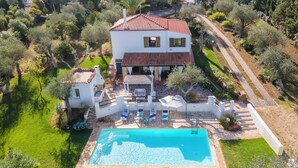 Une maison à deux étages avec une piscine, entourée d’une végétation luxuriante et bordée d’un chemin en pierre.