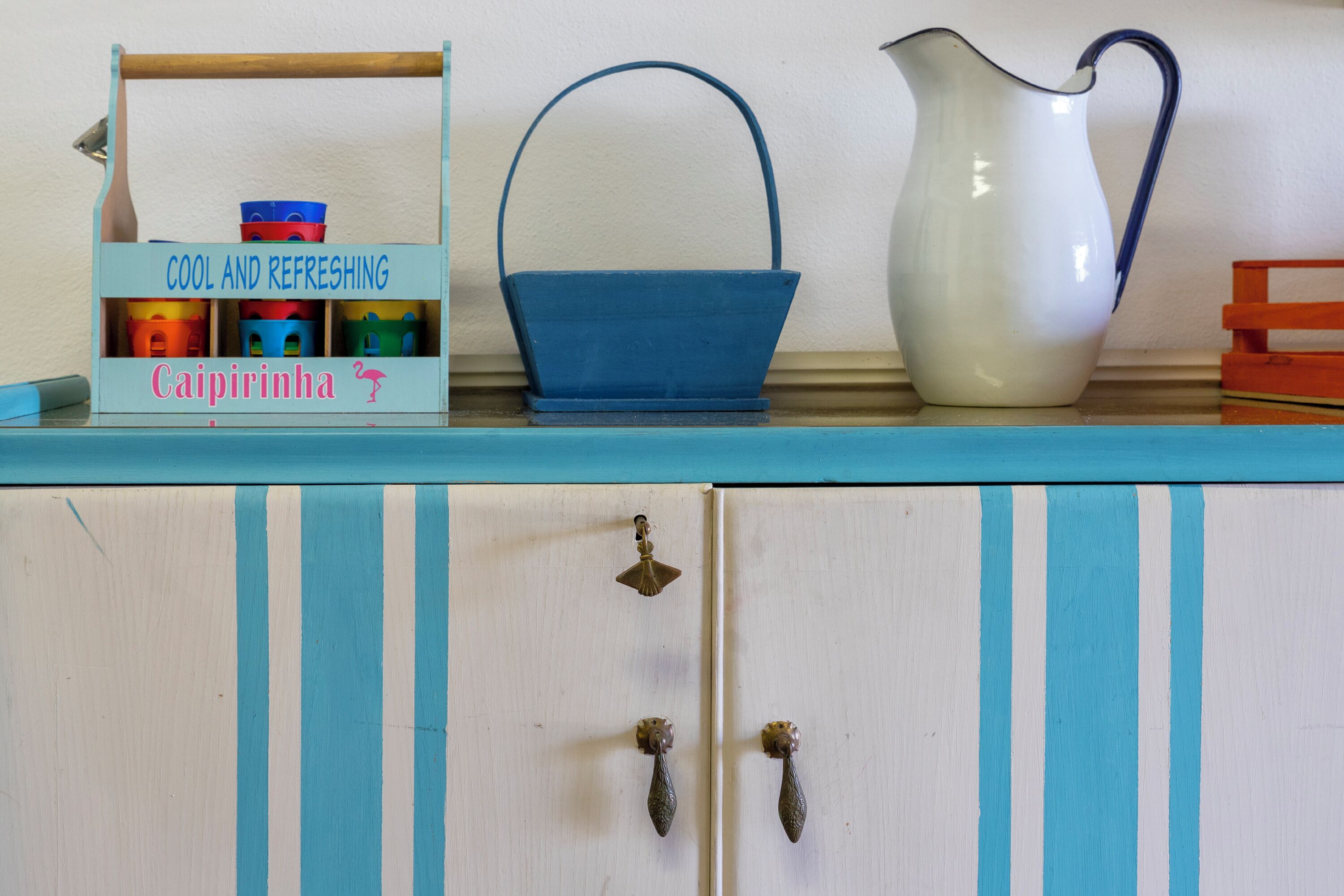 A kitchen counter with a blue and white striped cabinet, a blue basket, and a white pitcher.