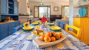 Un coin repas avec une table mise pour le petit-déjeuner, comprenant une variété de fruits, du pain et un vase de fleurs.