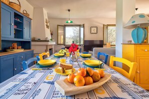 A dining area with a table set for breakfast, featuring a variety of fruits, bread, and a vase of flowers. - Villa Angiolina - Ideal for 5 people with A/C and Wi-Fi (Sardegna)