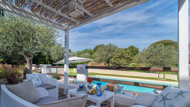 Une terrasse extérieure aménagée avec des meubles en osier, une piscine et une vue sur le paysage.