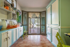A kitchen with a green chair, a white pitcher, and a blue bowl on the counter. - Villa Angiolina - Ideal for 5 people with A/C and Wi-Fi (Sardegna)
