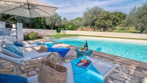Un espace aménagé au bord de la piscine, avec des chaises longues, une table sur laquelle est posé un magazine et une bouteille de vin.