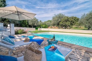 A poolside area with lounge chairs, a table with a magazine, and a bottle of wine. - Villa Angiolina - Ideal for 5 people with A/C and Wi-Fi (Sardegna)