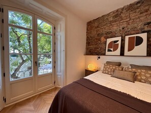 A bedroom with a large window, a brick wall, and a bed with multiple pillows. - Elegant 3BD Apartment in Malaga Plaza Marina II (Málaga)