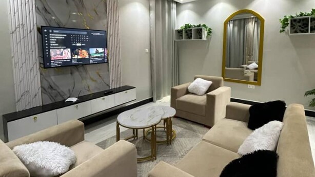 Een moderne woonkamer met een flatscreen televisie, beige banken, een salontafel en een accentmuur van marmer.