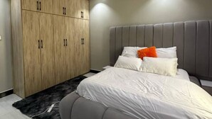 Een moderne slaapkamer met een groot bed, een grijs gestoffeerd hoofdeinde en een houten garderobe.