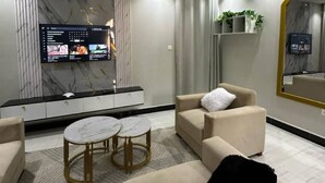 Een moderne woonkamer met een grote flatscreen televisie aan de muur, een bank, twee ronde salontafels en een decoratieve spiegel.
