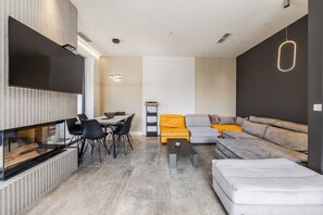 A modern living room with a flat-screen TV, a dining area with chairs, a sofa set, and a coffee table.
