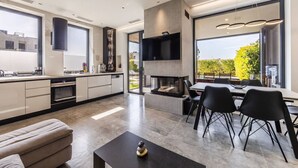 A modern kitchen with a built-in stove, dining area with black chairs, and a large window offering a view of greenery.
