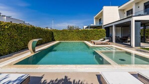 A modern pool with lounge chairs, a covered patio, and a white building with large windows.