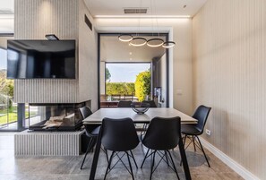 A modern dining area with a large table, black chairs, a fireplace, and a TV mounted on the wall.
