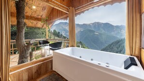 A wooden cabin with a large bathtub and a view of mountains.