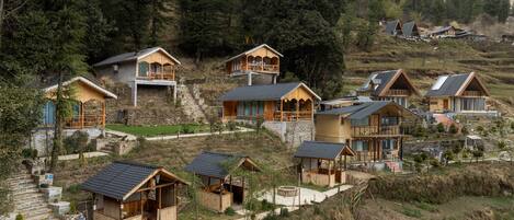 A cluster of wooden cabins with stone foundations, set on a hillside with a forest backdrop.