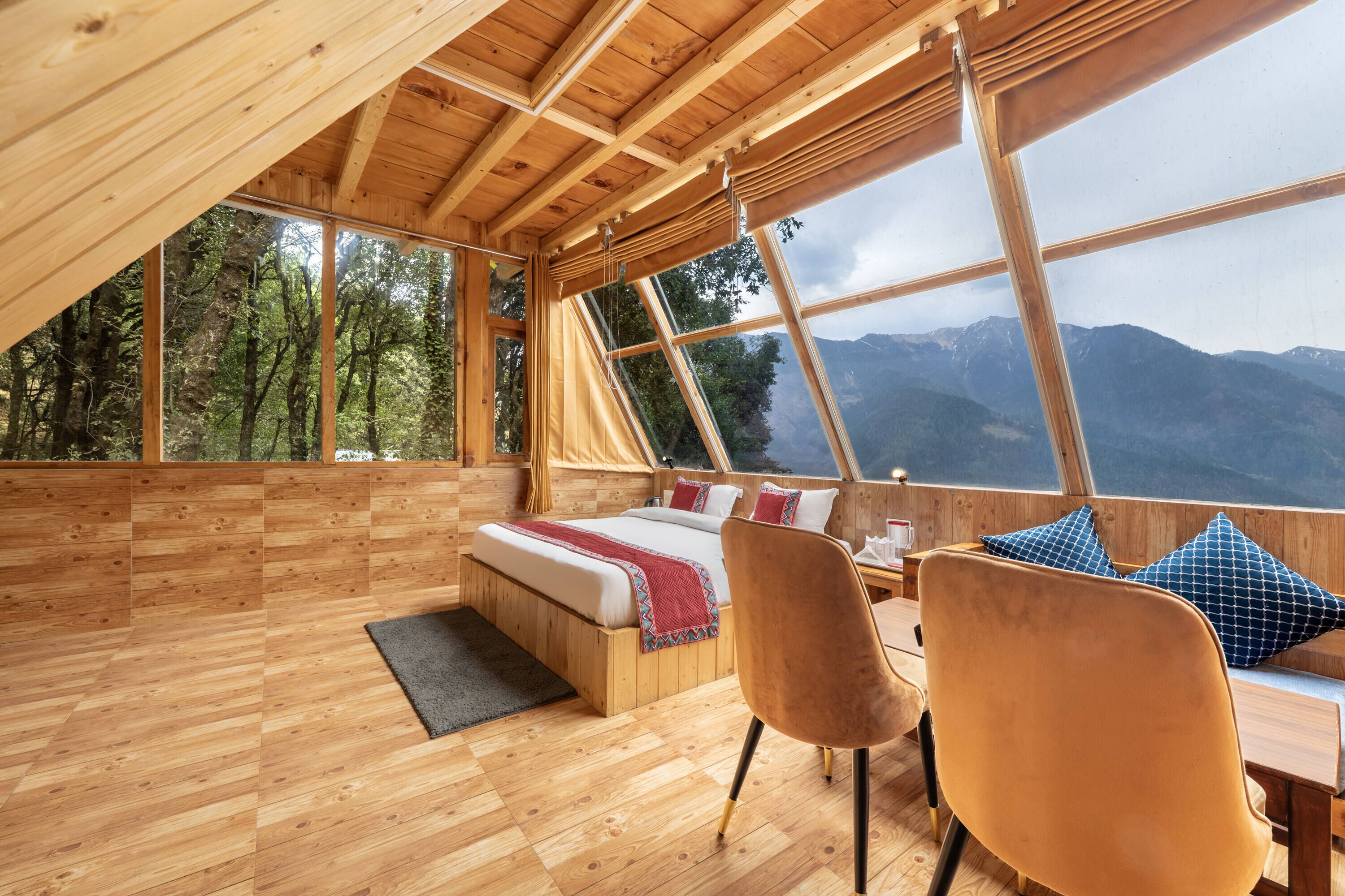 A wooden cabin with a bed, chairs, and a view of mountains.