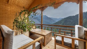 A wooden cabin with a balcony, a table, and two chairs.