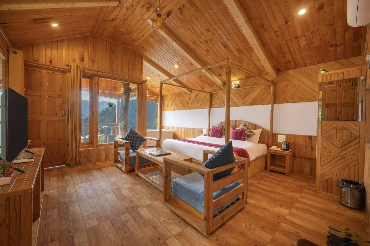 A wooden cabin interior with a bed, a desk, a chair, and a window with a view.