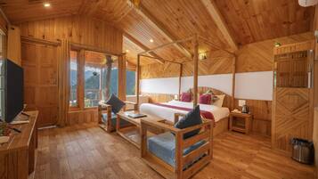A wooden cabin interior with a bed, a desk, a chair, and a window with a view.