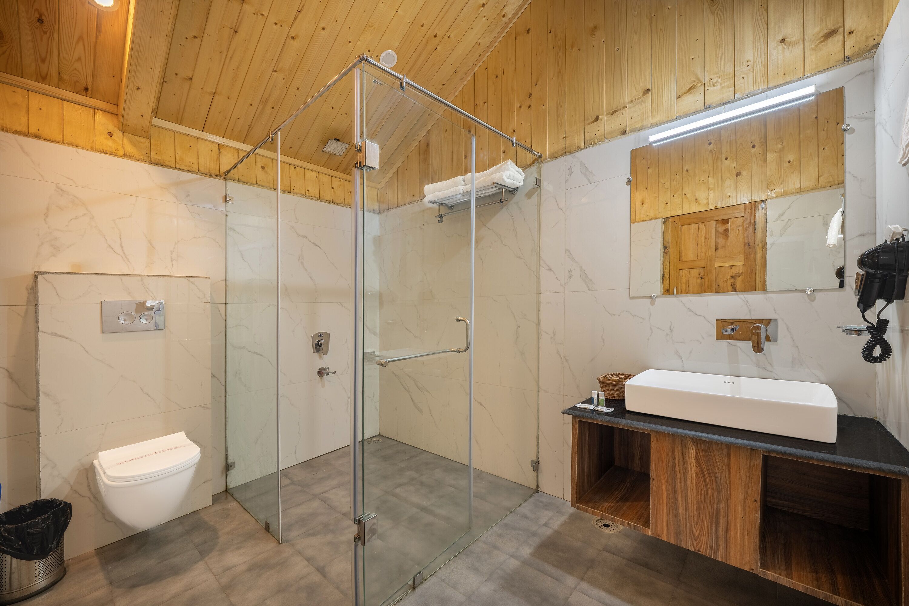 A modern bathroom with a glass-enclosed shower, a white toilet, and a wooden vanity with a sink.