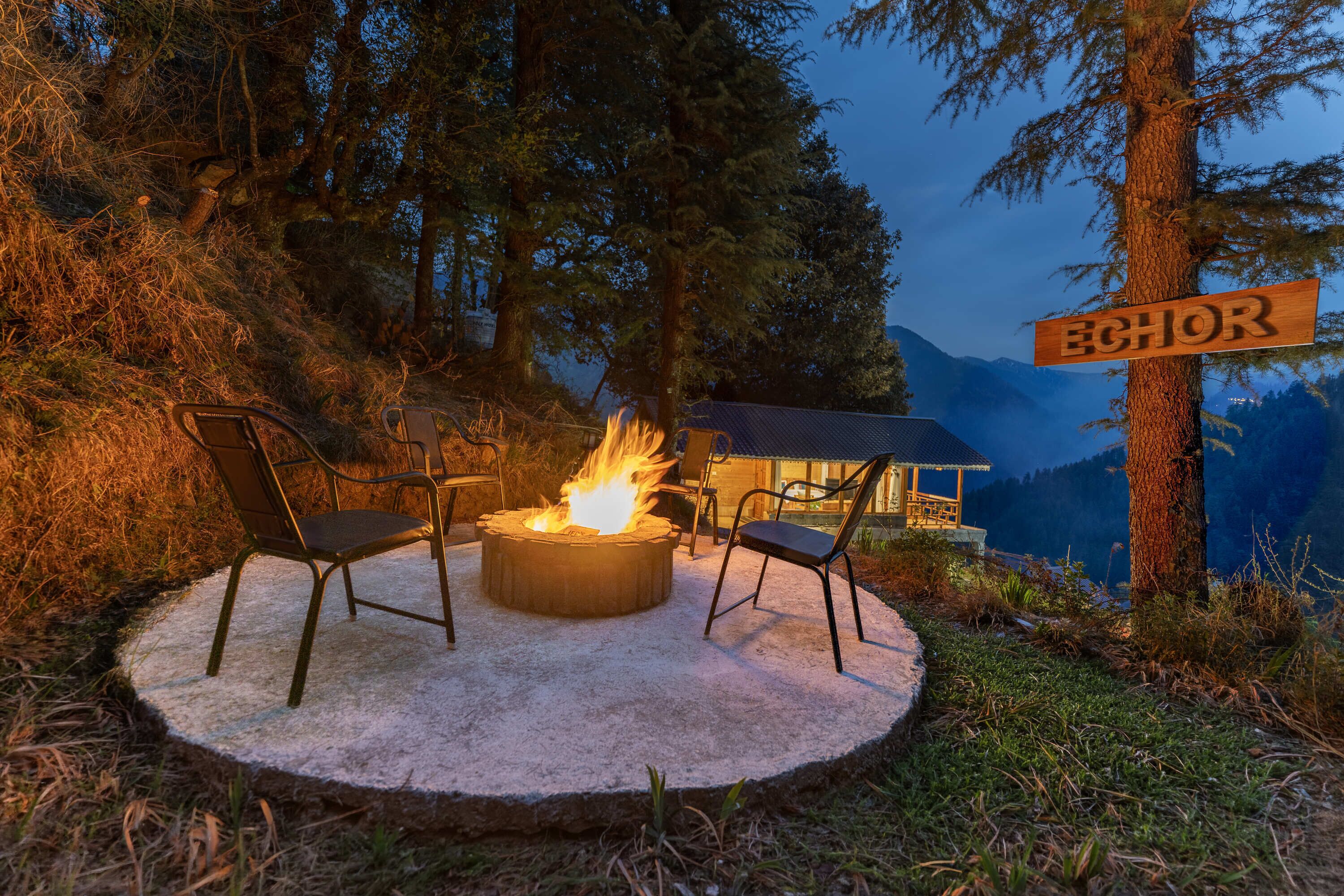 A circular outdoor seating area with a fire pit, two chairs, and a wooden sign reading 'ECHO.'