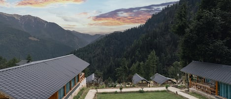 Un chalet de montagne doté d’une cour verdoyante, de cabanes en bois et offrant une vue sur des montagnes boisées.