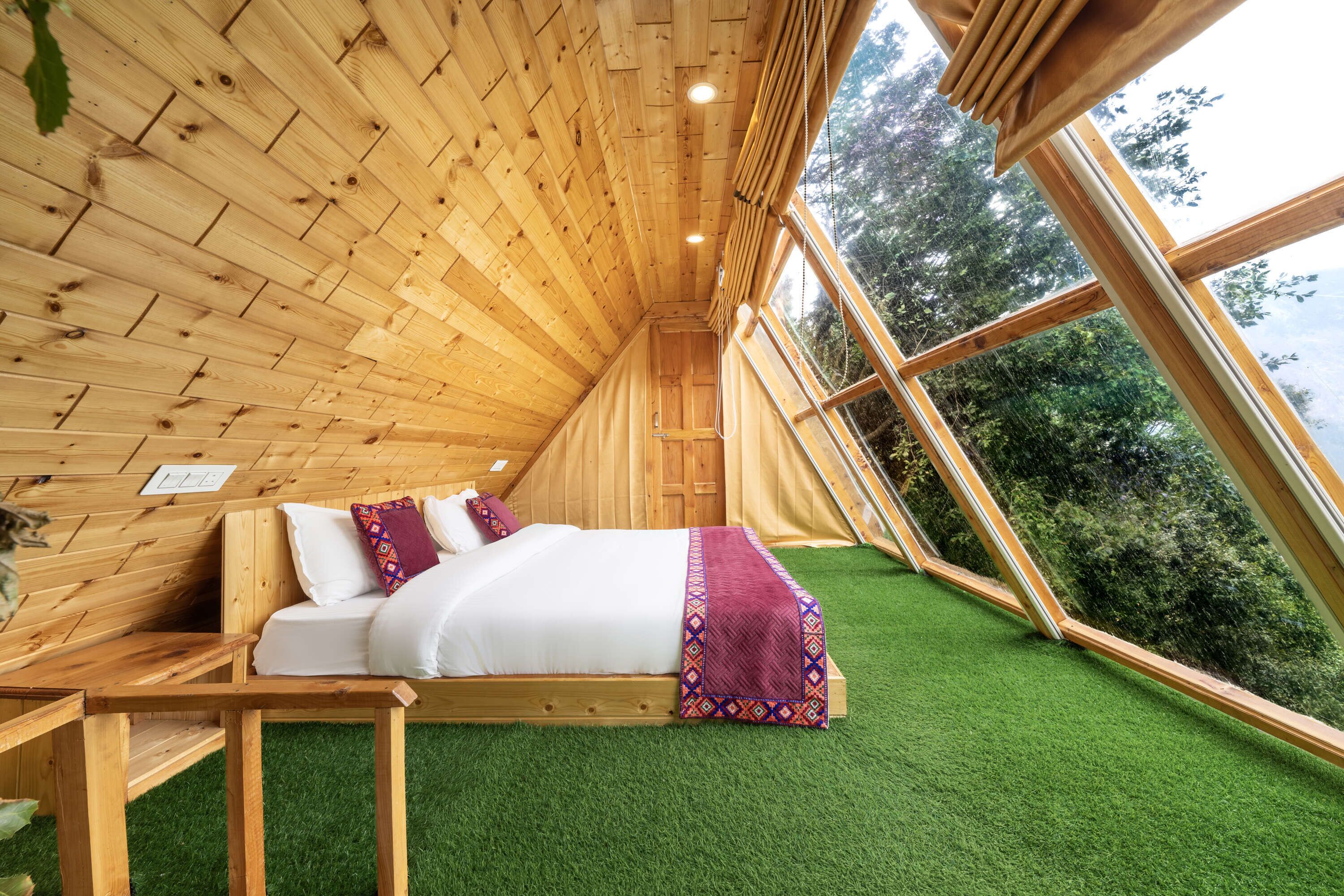 Una habitación de madera con una cama, una mesa y un ventanal.