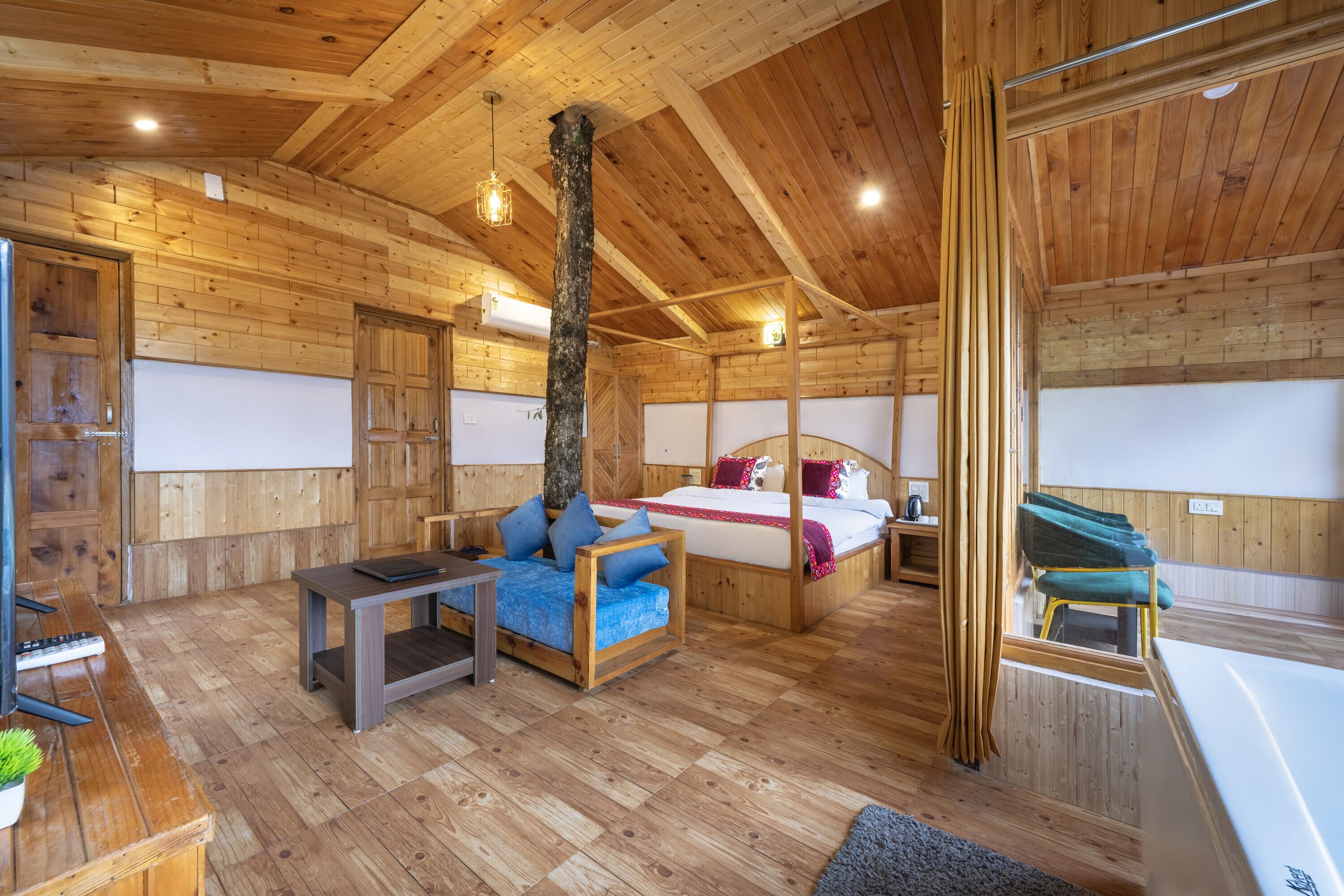 A wooden cabin interior with a bed, sofa, table, and a bathtub.