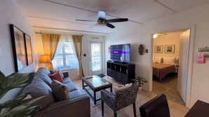 A living room with a sofa, a coffee table, a TV, and a ceiling fan. - Cozy Family Retreat - Steps to Beach - Pool - Hot Tub (South Padre Island)