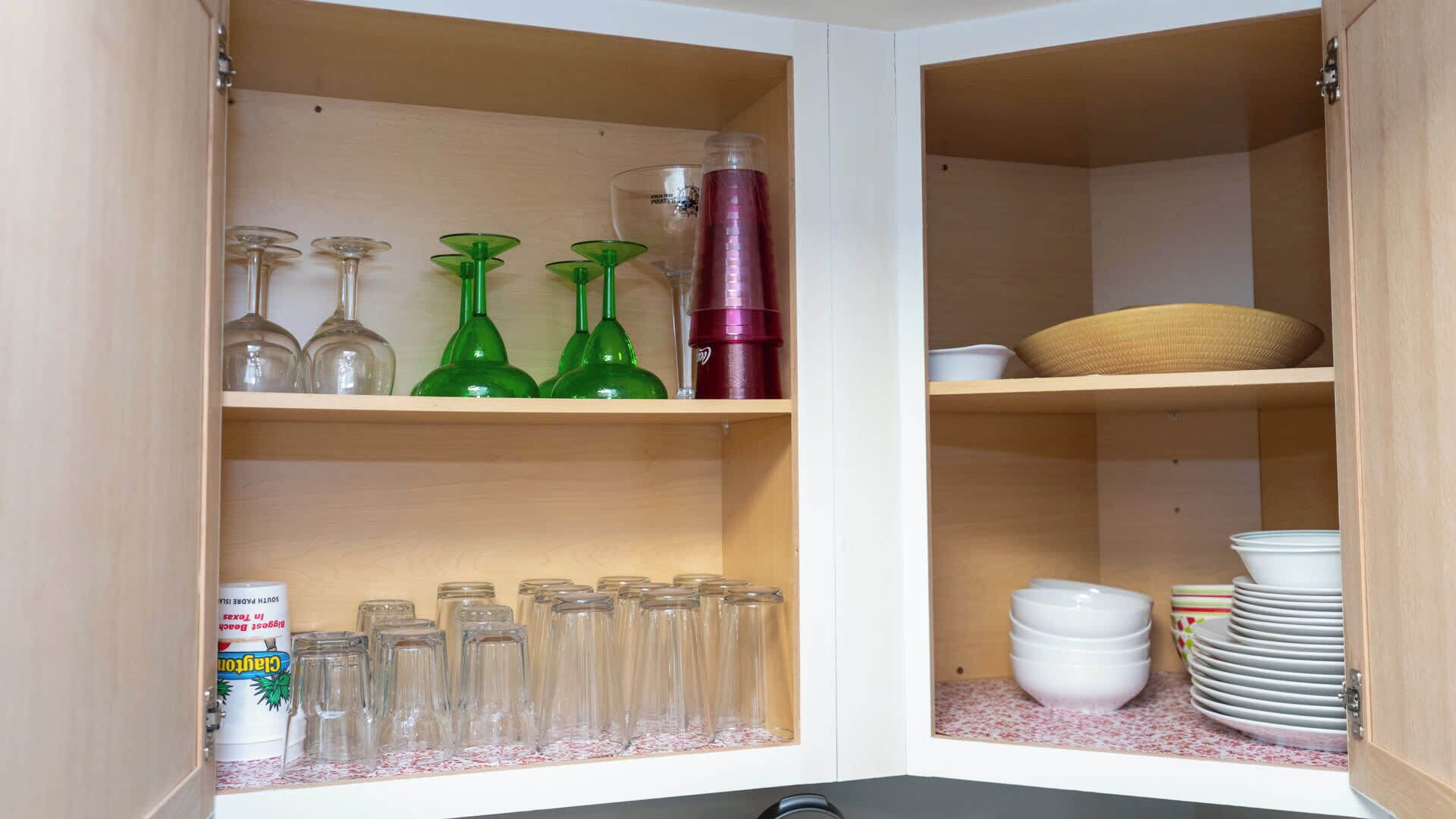 A kitchen cabinet with shelves containing glassware, a bottle, and a container.