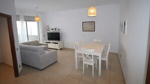 A modern living room with a sofa, TV, dining table, and chairs. - Panoramic B6 by Parc Mont-roig Apartment (Miami Playa)