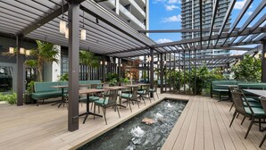 Een terras buiten met houten vloer, groene zitplaatsen en een klein waterpartij.