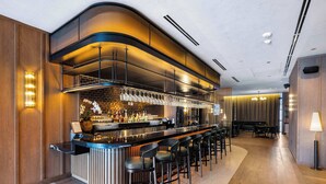 Een moderne bar met een gebogen toonbank, verschillende barkrukken en een divers assortiment flessen en glazen.