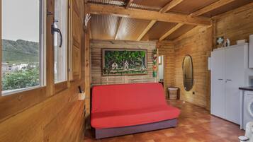 Un interior de madera con una cama, una lavadora y vistas por una ventana.