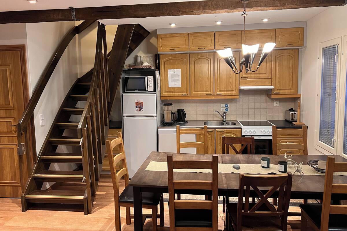 Une cuisine avec des meubles de rangement en bois, un four encastré, un four à micro-ondes, un évier et un coin repas comprenant une table et des chaises.