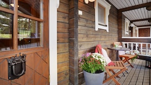 Een houten terras met een tafel en stoelen, een plant in pot en een hanglamp.